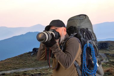 Sırt çantalı sakallı turist fotoğrafçı dağlardaki doğanın güzelliğini fotoğraflıyor. Dağlarda doğa yürüyüşleri