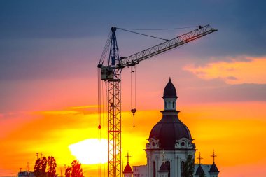 Günbatımına karşı inşaat vinci kullanan bir Hıristiyan kilise binası.