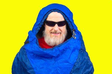 Sarı arka planda uyku tulumunda sakallı bir adam. Turizm ve seyahatte dinlenme ekipmanları