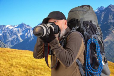 Sırt çantalı sakallı turist fotoğrafçı dağlardaki doğanın güzelliğini fotoğraflıyor. Dağlarda doğa yürüyüşleri