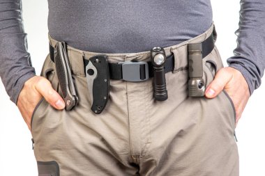 Katlanan bıçak ve turist yürüyüş pantolonunun kemerinde klipsleri olan bir el feneri. EDC ögeleri