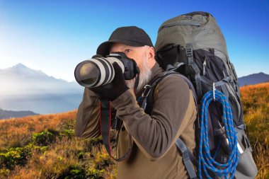 Sırt çantalı sakallı turist fotoğrafçı dağlardaki doğanın güzelliğini fotoğraflıyor. Dağlarda doğa yürüyüşleri