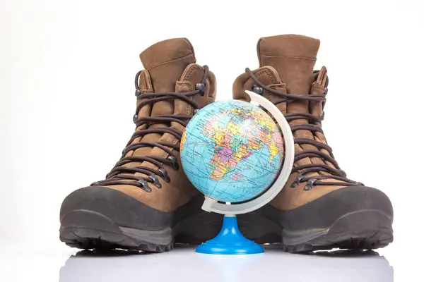 Trekking boots for hiking next to a world globe model on a white background. Equipment for travel and hiking