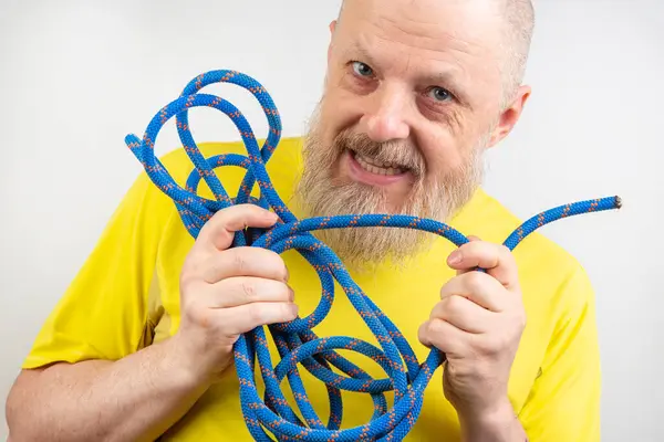 strong colored rope for climbing equipment in the hand of a bearded man in a yellow T-shirt on a light background. item for tourism and travel