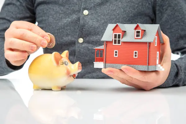 piggy bank with money and a model of a house in the hands of a man. the concept of accumulating finance to buy a house