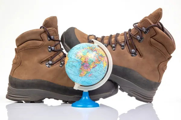 Trekking boots for hiking next to a world globe model on a white background. Equipment for travel and hiking