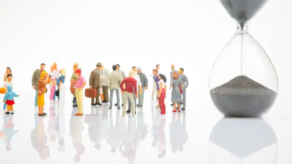 miniature people. group of different people stand near an hourglass against a white background. concept of people life time in society.