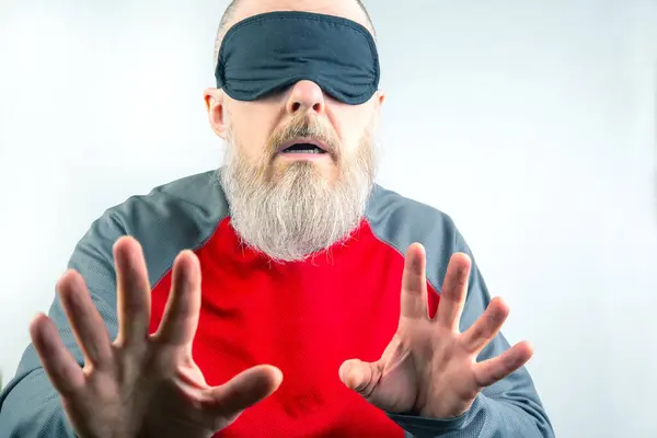Bearded man wearing a blindfold for sleeping. Concept of a blind man searching in the dark