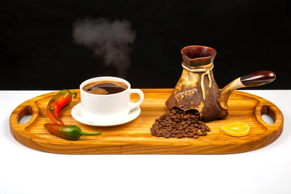 Freshly brewed hot black coffee in a white cup on a wooden board next to a ceramic turkey with coffee beans.