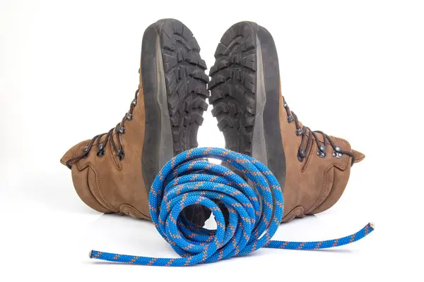 Beyaz arka planda tırmanma ipinin yanında yürüyüş botları. Seyahat ve Yürüyüş Ekipmanı