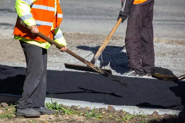 工人们把新鲜的沥青铺在人行道上 道路业 免版税图库图片
