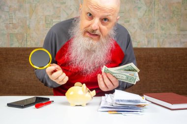 Sakallı kıdemli adam, emeklilik birikimlerinin ve bütçe hesaplamalarının zorluklarını sembolize eden finansal dökümanlar ve kumbaralarla çevrili parasını dikkatle sayıyor.