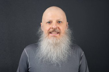 Uzun, beyaz sakallı, esmer bir arka plana gülümseyen yaşlı bir adam. Parlak gözleri ve kel kafası neşeli ve arkadaş canlısı tavrını vurguluyor.