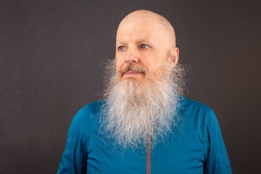 Koyu gri arka planda büyük gri sakallı mutlu bir kel adamın portresi.