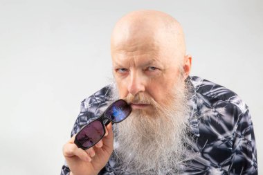 Geniş gri sakallı, açık arkaplanda güneş gözlüğü takan başarılı bir kel adam portresi..