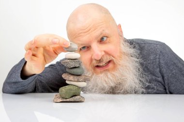 Neşeli bir ifadeyle yaşlı bir adam doğal taşlardan oluşan bir koleksiyonu istifleyerek huzurlu bir farkındalık anını, yaratıcılığı ve kayaları meditasyon ortamında dengeleme sanatını resmediyor.