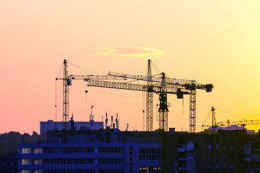 Günbatımı gökyüzünün arka planında inşa edilmiş evler olan vinçler.