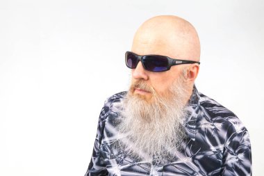 Geniş gri sakallı, açık arkaplanda güneş gözlüğü takan başarılı bir kel adam portresi..