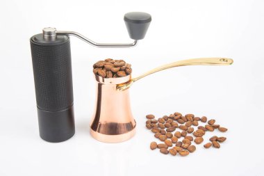 Pürüzsüz, sade bir kahve öğütücüsünün yakın plan çekimi, geleneksel bir bakır çakmak ve kahve çekirdekleri beyaz bir yüzeye yayılmış, kahve hazırlama fotoğrafçılığı için ideal..