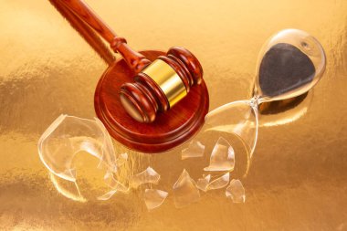 Kanuni otoritenin kesişmesini ve zamanın geçiciliğini temsil eden, üzerinde siyah kum bulunan, altın bir yüzey bulunan kırık bir kum saatinin yanındaki parlak tokmağın yakın çekimi..