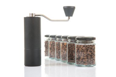 Kahve çekirdekleri için siyah manuel kahve öğütücüsü ve siyah kahve çekirdekleri ile dolu altı bardak şeffaf kavanoz ve beyaz arka planda kahve demlemek için toprak takımı..