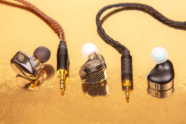 Yansıtıcı altın bir yüzey üzerinde dokuma kablo ve altın kaplamalı üç kulaklık, teknoloji ürünü çekimleri ve ses aksesuarları için ideal..