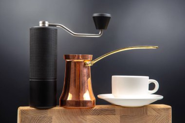 Modern bir manuel kahve öğütücüsü, bakır Türk çakmağı, ve ahşap bir yüzey üzerinde beyaz seramik bardak, sıcak bir kahve havası için koyu mavi arka planda yakalanmış..