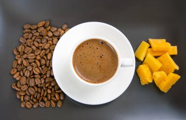 Kahve fincanında beyaz bir fincanda espresso, peynir çubukları ve kahve çekirdekleri koyu bir yüzeye yayılmış, sıcak bir sabah titreşimini vurguluyor..