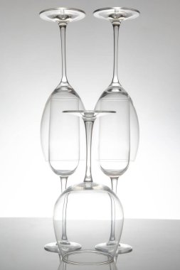 Zarif sapları düzgün sıralanmış, parlak bir masaya yansıyan zarif boş şarap kadehleri sofistike dekorlar için minimalist gri bir zemin üzerine kurulmuş..