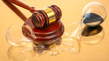 Kanuni otoritenin kesişmesini ve zamanın geçiciliğini temsil eden, üzerinde siyah kum bulunan, altın bir yüzey bulunan kırık bir kum saatinin yanındaki parlak tokmağın yakın çekimi..