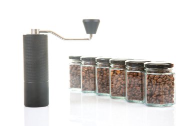 Kahve çekirdekleri için siyah manuel kahve öğütücüsü ve siyah kahve çekirdekleri ile dolu altı bardak şeffaf kavanoz ve beyaz arka planda kahve demlemek için toprak takımı..