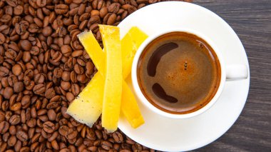 Peynir çubuklarıyla bembeyaz bir fincanda zengin espresso, ahşap bir yüzeyde kahve çekirdekleri arasına yerleştirilmiş, gurme kahvaltısı için mükemmel..