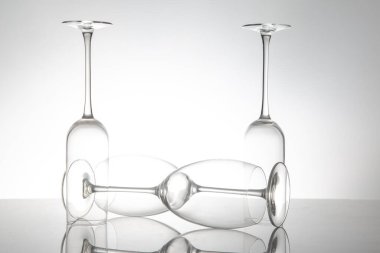 Zarif şekilli ve saplı beş boş şarap kadehi, parlak bir yüzeyde yansımaları iki katına çıkıyor, lüks temalar için yumuşak gri bir zemin üzerine kurulmuş..