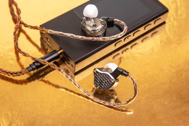 Parlak, siyah bir ses oynatıcının üzerinde dokuma kablosu olan kablolar, yansıtıcı altın bir yüzeye kurulmuş. Teknoloji, ses ve modern tasarım kavramları için ideal.