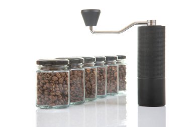 Kahve çekirdekleri için siyah manuel kahve öğütücüsü ve siyah kahve çekirdekleri ile dolu altı bardak şeffaf kavanoz ve beyaz arka planda kahve demlemek için toprak takımı.