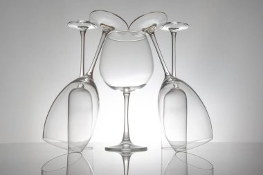 Zarif şekilli ve saplı beş boş şarap kadehi, parlak bir yüzeyde yansımaları iki katına çıkıyor, lüks temalar için yumuşak gri bir zemin üzerine kurulmuş..