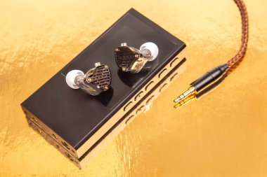 Sade siyah bir müzik çaların üzerinde örülmüş kabloyla kablolu kulaklıklar, altın bir yüzeye yansıyor. Teknoloji, ses ve minimalist tasarım stok fotoğrafçılığı için mükemmel..