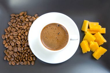 Beyaz bir fincanda espresso, peynir çubukları ve siyah bir masada kavrulmuş kahve çekirdekleri olan minimalist bir sahne. Yemek fotoğrafçılığı için ideal.