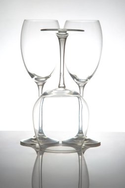 Uzun saplı üç zarif, boş şarap kadehinden oluşan gösterişli bir sıra, yumuşak gri arka planda parlak bir yüzeye yansıyor, yemek ya da olay temaları için mükemmel..