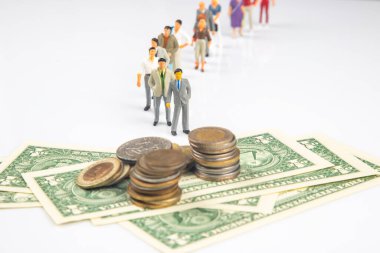 Bozuk paralar ve dolar banknotları ile eşleştirilmiş bulanık bir arka plana karşı bir kuyruk oluşturan minyatür insanlar, para, iş veya sosyal eşitsizliği temsil eden kavramsal bir kurulum