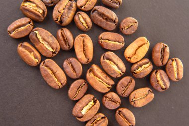 Kavrulmuş kahve çekirdeklerinin detaylı görüntüsü, koyu arkaplandaki sıcak kahverengi gölgeleri ve doğal çatlakları vurguluyor. Kafeinle ilgili projeler için uygundur.