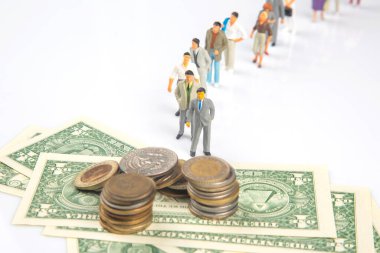 İnsanların minyatür figürlerinin ön planda para yığınları ve Amerikan doları banknotlarıyla bir arada durduğu yaratıcı bir kompozisyon, mali hiyerarşiyi veya ekonomik kavramları sembolize ediyor