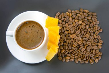 Kahve fincanında beyaz bir fincanda espresso, peynir çubukları ve kahve çekirdekleri koyu bir yüzeye yayılmış, sıcak bir sabah titreşimini vurguluyor..