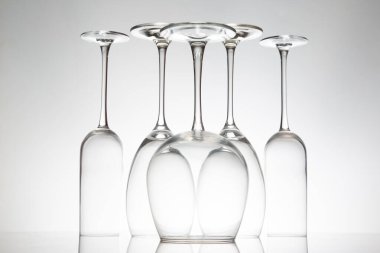 Zarif sapları düzgün sıralanmış, parlak bir masaya yansıyan zarif boş şarap kadehleri sofistike dekorlar için minimalist gri bir zemin üzerine kurulmuş..