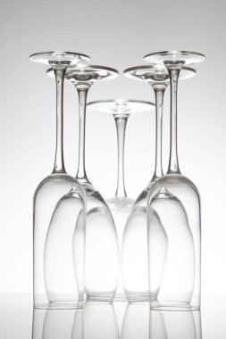 Kristal şarap kadehleri çeşitli şekillerde dimdik durur, yansımaları parlak bir yüzeyde ikiye katlanır, güzel yemek kavramları için yumuşak gri bir zemin üzerine yakalanır..