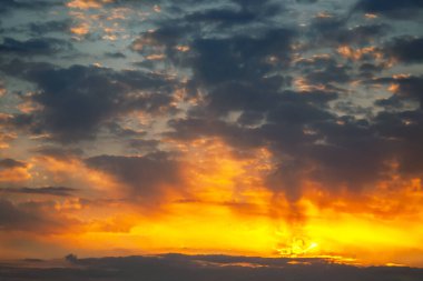 Ufukta parlak bir gün batımı turuncu, pembe ve mavi renklerden oluşan renkli bir gökyüzü. Dağınık bulutlar güneş ışığını yansıtıyor, sakin ve resimsel bir sahne yaratıyor, doğa için mükemmel.