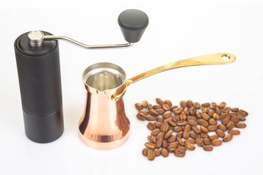 Pürüzsüz, sade bir kahve öğütücüsünün yakın plan çekimi, geleneksel bir bakır çakmak ve kahve çekirdekleri beyaz bir yüzeye yayılmış, kahve hazırlama fotoğrafçılığı için ideal..