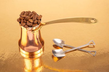 Altın bir yüzey üzerinde kahve çekirdeği yığını ile birlikte pirinç saplı cilalı bakır bir mağara, geleneksel kahve demleme ve yaşam tarzı temaları için mükemmel.