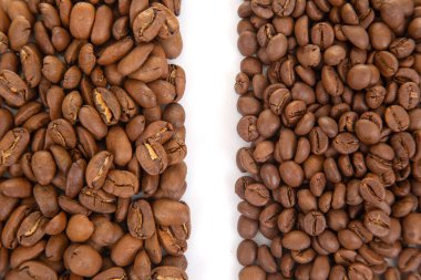 Kavrulmuş kahve çekirdeklerini yakın plan beyaz zemin üzerinde iki tonda, toprak renklerini ve çatlak yüzeylerini vurgulayarak. Gurme kahve görselleri için mükemmel.