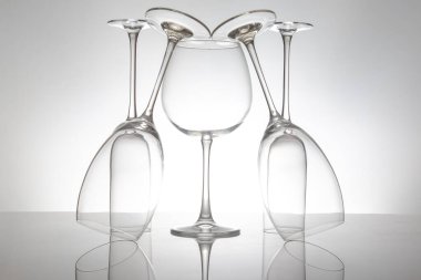 Zarif şekilli ve saplı beş boş şarap kadehi, parlak bir yüzeyde yansımaları iki katına çıkıyor, lüks temalar için yumuşak gri bir zemin üzerine kurulmuş..